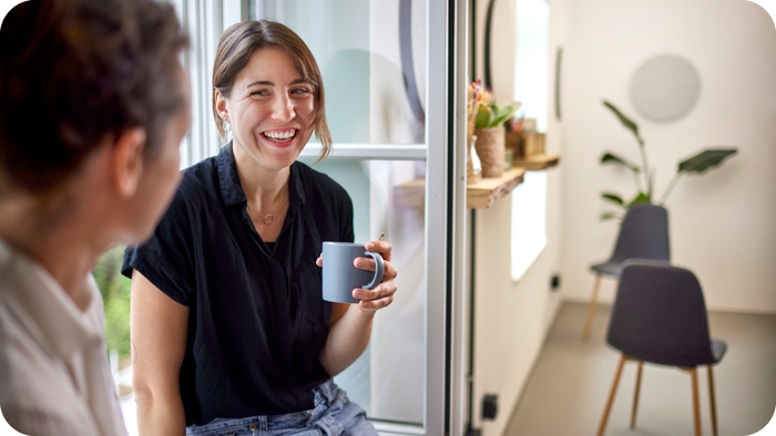 Bilde av blid dame med kaffekopp som fører samtale med en jobbkollega.